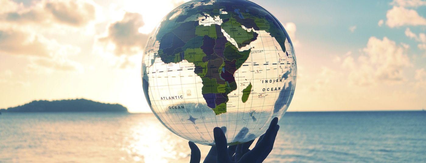 Hands holding a globe above the ocean